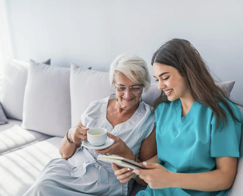 A caregiver in teal scrubs sharing a calm, supportive moment with an older woman at home.